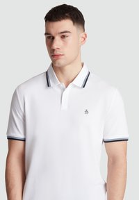 Witte polo met marineblauwe streepaccenten langs de kraag en mouwen. Heeft een geborduurd pinguïnlogo op de linkerborst. Korte mouwen.