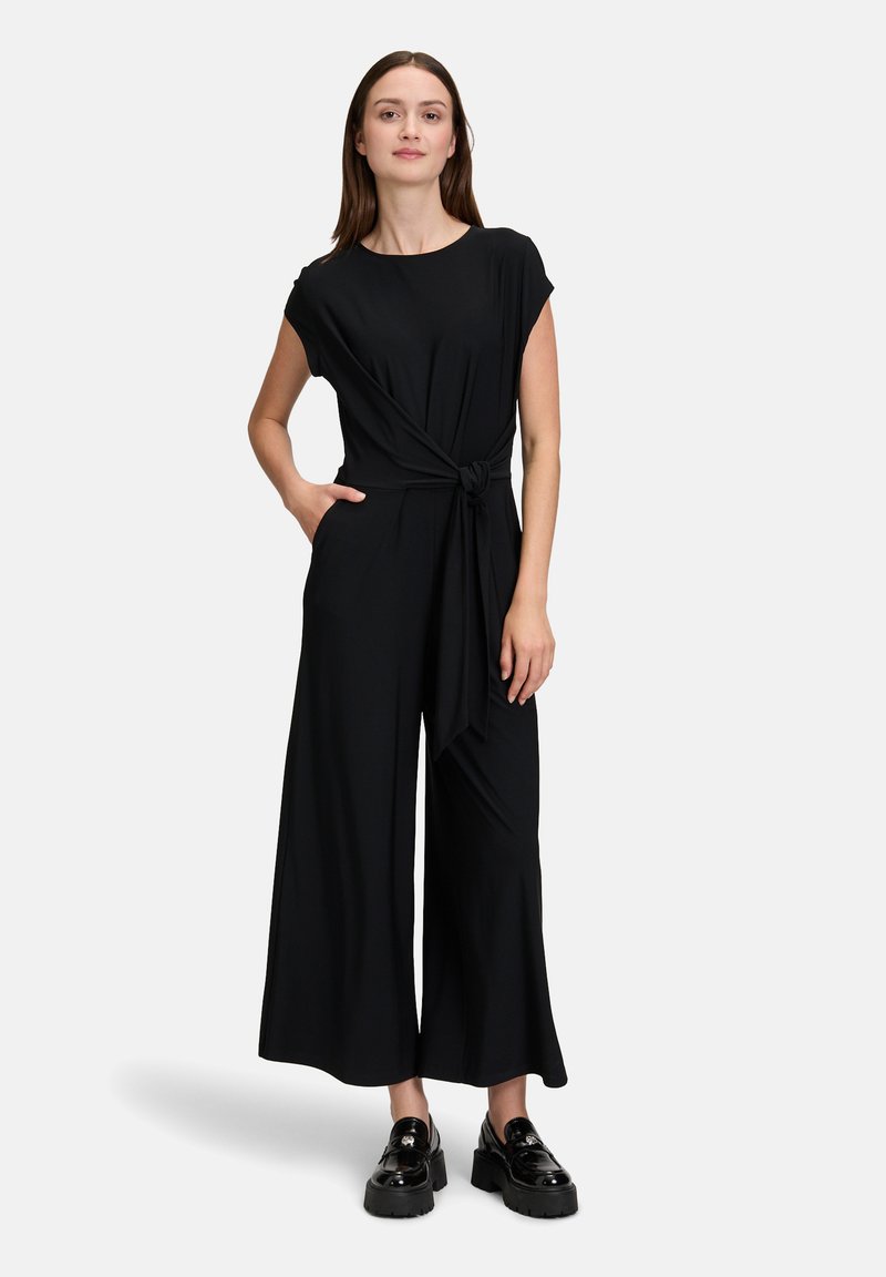 Zwarte jumpsuit met een ronde halslijn, korte mouwen, een geknoopt taille detail en wijd-uitlopende broekspijpen. Glad materiaal met een vloeiende textuur.