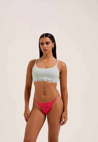 Ανοιχτό μπλε crop top με λωρίδα λογότυπου και ροζ στρινγκ με κείμενο. Μαλακό ύφασμα, εφαρμοστή γραμμή και ελάχιστη κάλυψη με ρυθμιζόμενες τιράντες.