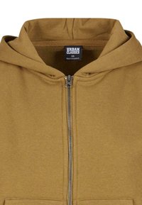 Felpa con zip marrone, dal texture morbido, con cappuccio e zip frontale. Presenta un'etichetta interna che indica la taglia (XS) e il paese di fabbricazione.