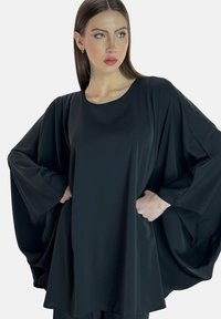 Túnica negra de corte holgado, mangas amplias estilo murciélago, textura suave, escote redondo y silueta fluida. Diseño simple y elegante.