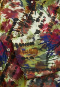 Chemise boutonnée en tissu léger avec un motif abstrait multicolore comprenant des nuances de rouge, vert, bleu et noir. Les boutons sont blancs.