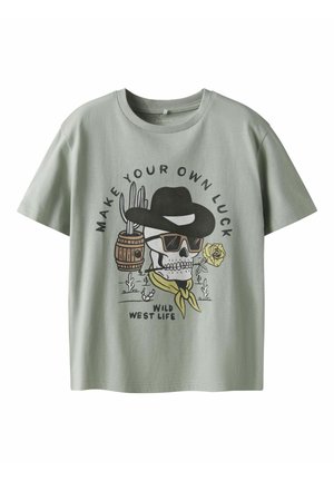 Vaaleanvihreä lyhythihainen T-paita, joka on valmistettu puuvillasta. Paidan etuosassa on painettu kuvio, jossa on pääkallo cowboy-hatussa ruusun kanssa, ympärillä koristeellisia elementtejä.