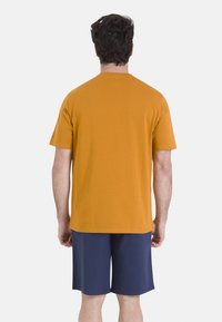 T-shirt à manches courtes jaune moutarde avec un col rond, associé à un short bleu marine, vu de dos, texture de tissu lisse.