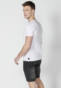 Short-sleeve white cotton t-shirt featuring red accent stitching, paired with dark denim shorts with side pockets and rolled hems.