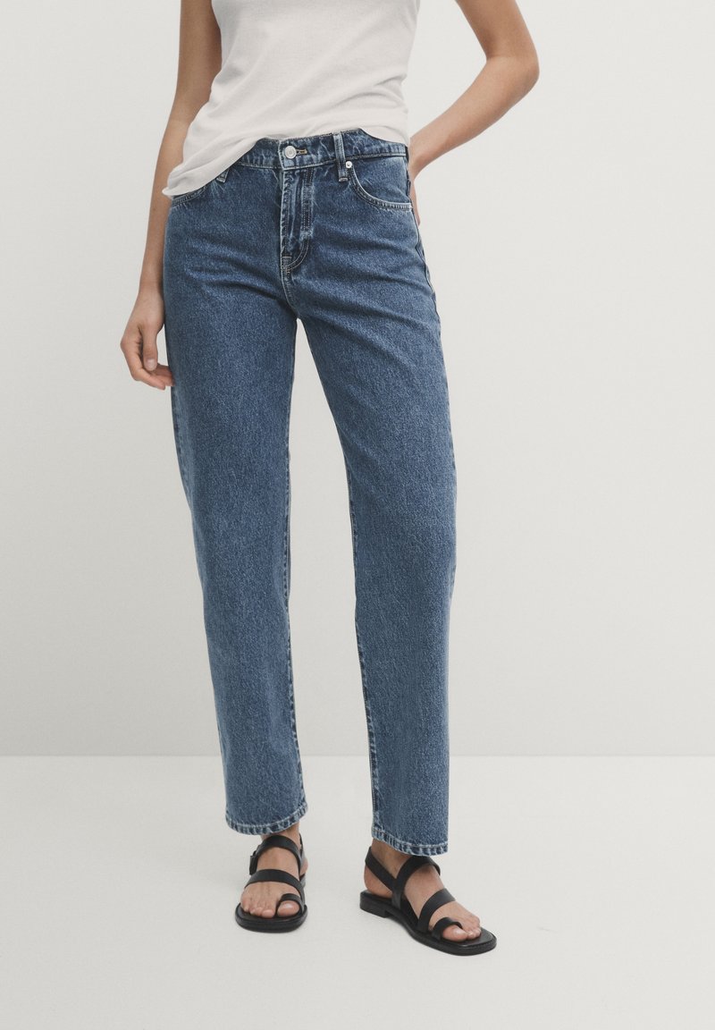 Blå högmidjade raka jeans i denim, med knappstängning fram, fem fickor och en något urblekt finish. Svarta remsandaler.