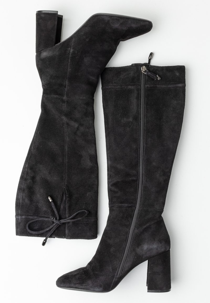 Pari korkeavartisia mustia mokka-saappaita, joissa on paksut korot, sivuvetoketjut ja koristeellinen ruusu takana yläreunassa valkoista taustaa vasten.