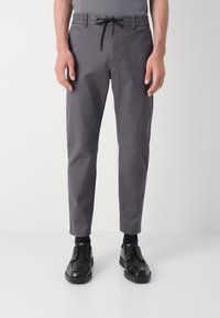 Grå, avsmalnande byxor med elastisk midjeband och dragsko; kombinerade med svarta snörskor och mörka strumpor.