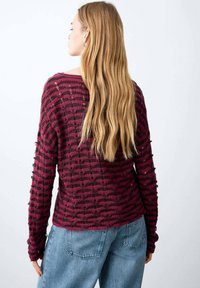 Pulover bordo cu mâneci lungi și dungi orizontale negre, cu o țesătură texturată și croială lejeră, purtat împreună cu blugi albaștri cu talie înaltă.