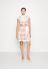 Robe florale rose avec corsage en dentelle, manches courtes et ceinture en satin. Dispose d'une jupe évasée et d'une broderie ton sur ton. Assortie avec des talons nude.