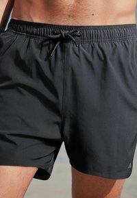 Schwarze Badeshorts aus leichtem, glattem Stoff. Mit einem Kordelzugbund und einem Logo-Akzent auf der unteren linken Seite.