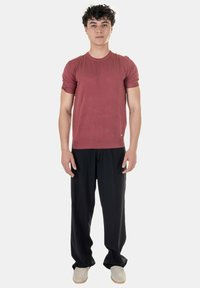 T-shirt rossa in cotone con maniche corte, abbinata a pantaloni neri larghi. Il modello si trova in posizione eretta su uno sfondo neutro.