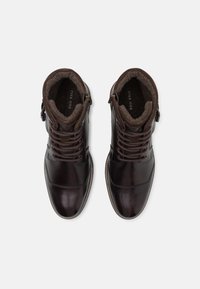 Botas de cuero marrón con cordones y un acabado suave, con cuello acolchado y forro interior de forro polar. Presentan una cremallera lateral y costuras en contraste.