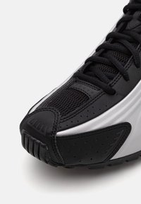 Baskets noires et blanches vues de face avec des empiècements en mesh et synthétiques, lacets noirs et semelle en caoutchouc texturée sur fond blanc.