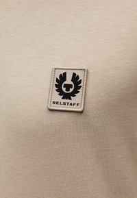 Μπεζ βαμβακερό μπλουζάκι με μαύρο κεντημένο λογότυπο Belstaff σε ορθογώνιο έμβλημα. Λείο ύφασμα με εφαρμοστή γραμμή.