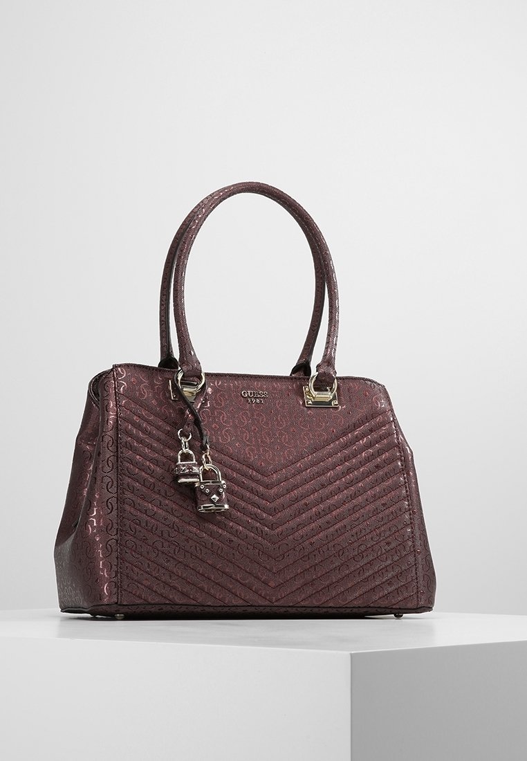 Sac à main Guess violet foncé avec deux poignées, texture matelassée en chevrons, logo en métal, et deux petits charms cadenas attachés.