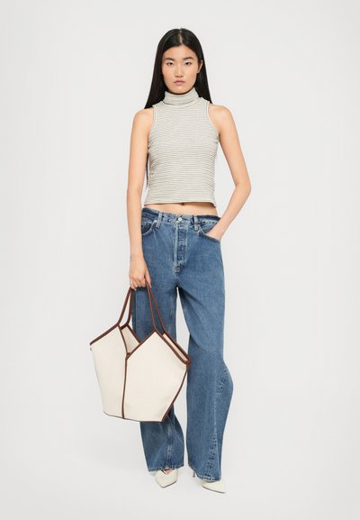 White and brown tote bag with geometric design, paired with a grey striped sleeveless top and light blue wide-leg jeans.