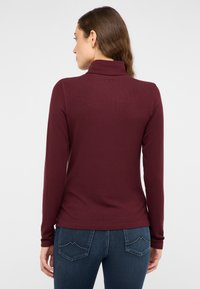 Bordowa, długorękawowa góra z golfem o prążkowanej fakturze; dopasowany krój. Połączona z ciemnoniebieskimi jeansami z ozdobnym przeszyciem na tylnej kieszeni.
