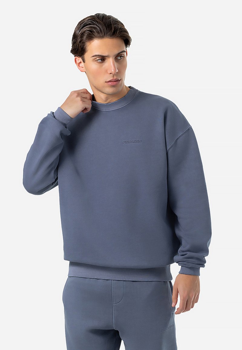 Blå sweatshirt med rund halsudskæring, blød tekstur og ribbede manchetter. Har et subtilt præget logo på brystet. Koordineret med matchende bukser.