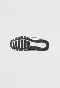 Podošva bežeckej obuvi Nike v čiernej farbe s textúrovaným gripom, s flex grooves pre flexibilitu. Biela medzipodrážka s detailom loga.