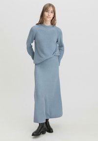 Hellblau gestrickter Sweater mit Rippenmuster und passendem langem Rock in lockerer Passform. Schwarze Knöchelstiefel runden das Outfit ab.