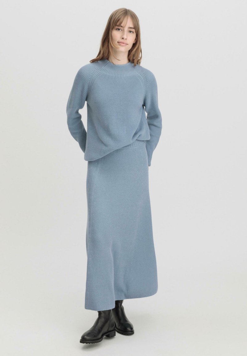 Hellblau gestrickter Sweater mit Rippenmuster und passendem langem Rock in lockerer Passform. Schwarze Knöchelstiefel runden das Outfit ab.