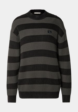 Suéter a rayas en gris y negro. Textura acanalada, cuello redondo, mangas largas, con un parche de logo en el pecho.