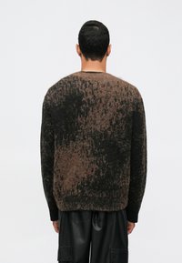 Textúrált pulóver sötétbarna és fekete árnyalatokban, laza szabással, kerek nyakkal és hosszú ujjal. Puha, bolyhos anyag.