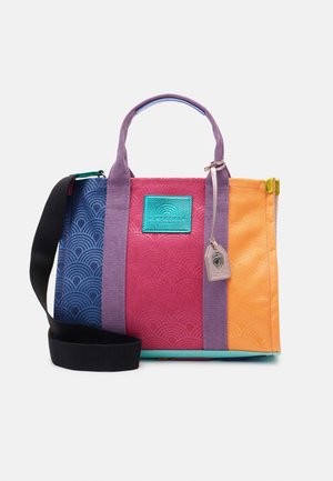 Bunte Tragetasche mit blauen, pinken und orangen Paneelen, violetten Griffen, schwarzem verstellbarem Schultergurt und einem kleinen angehängten Etikett.