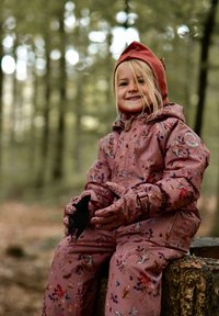 Roosa lillemustriga isoleeritud lumepesu koos sobivate kinnastega, millel on kapuuts, paigutatud kändu peale metsas.