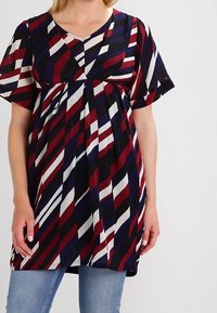 Monivärinen tunika V-päällä ja lyhyillä hihoilla. Siinä on vaakasuora raitakuvio punaisena, tummansinisenä ja valkoisena. Löysä malli, teksturoitu kangas.