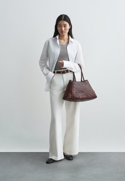Λευκό πουκάμισο πάνω από γκρι tank top, συνδυασμένο με ψηλοκάβαλες λευκές παντελόνες και μαύρες γόβες. Μια πλεκτή σκούρα καφέ τσάντα ολοκληρώνει την εμφάνιση.