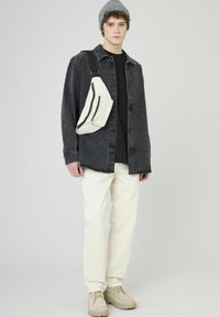 Chemise en denim noire portée sur un t-shirt noir, pantalon crème et chaussures beiges. Un sac bandoulière de couleur claire avec un détail zippé est porté en travers du corps.