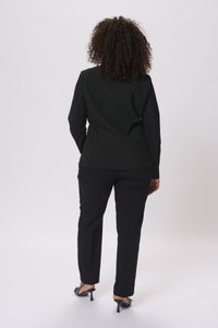 Černý saka a kalhoty na míru s hladkou texturou, se štíhlým střihem a jednoduchým designem. Černé lodičky na vysokém podpatku dotvářejí celý outfit.