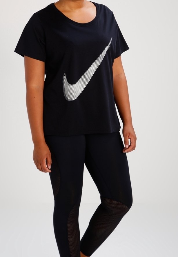 Musta puuvillapaita, jossa on suuri valkoinen Nike-merkki, yhdistettynä mustiin leggings-haalareihin, joissa on verkkopaneelit ja tiukka muotoilu.