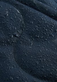 Tissu foncé avec des gouttelettes d'eau perlant à la surface, montrant une texture et des détails de matériau résistants à l'eau.