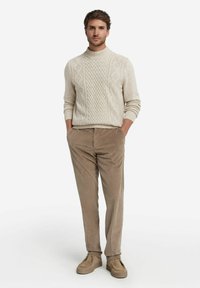 Kremowy sweter dzianinowy z wysokim kołnierzem i wzorem w warkocze, zestawiony z jasnobrązowymi spodniami z korduroju i dopasowanymi beżowymi butami wsuwanymi.