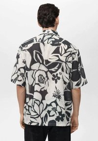 Kurzarmhemd mit einem schwarz-weißen Blumenmuster, relaxter Passform und leichtem Stoff. Rückansicht gezeigt.