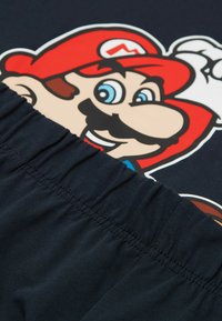 Schwarzes T-Shirt mit einem bunten Grafikdesign eines Cartoon-Charakters mit rotem Hut und Schnurrbart; das Shirt hat einen gerafften Ausschnitt und eine weiche Textur.