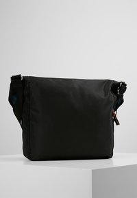 Borsa a tracolla in tessuto nero con cintura regolabile, texture liscia e design minimalista; presenta dettagli hardware sottili.