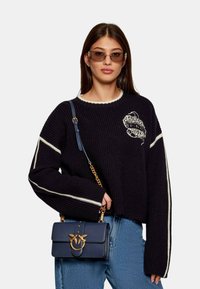 Maglione lavorato a maglia navy con strisce bianche e design ricamato, abbinato a una borsa strutturata navy con hardware dorato e tracolla a catena.