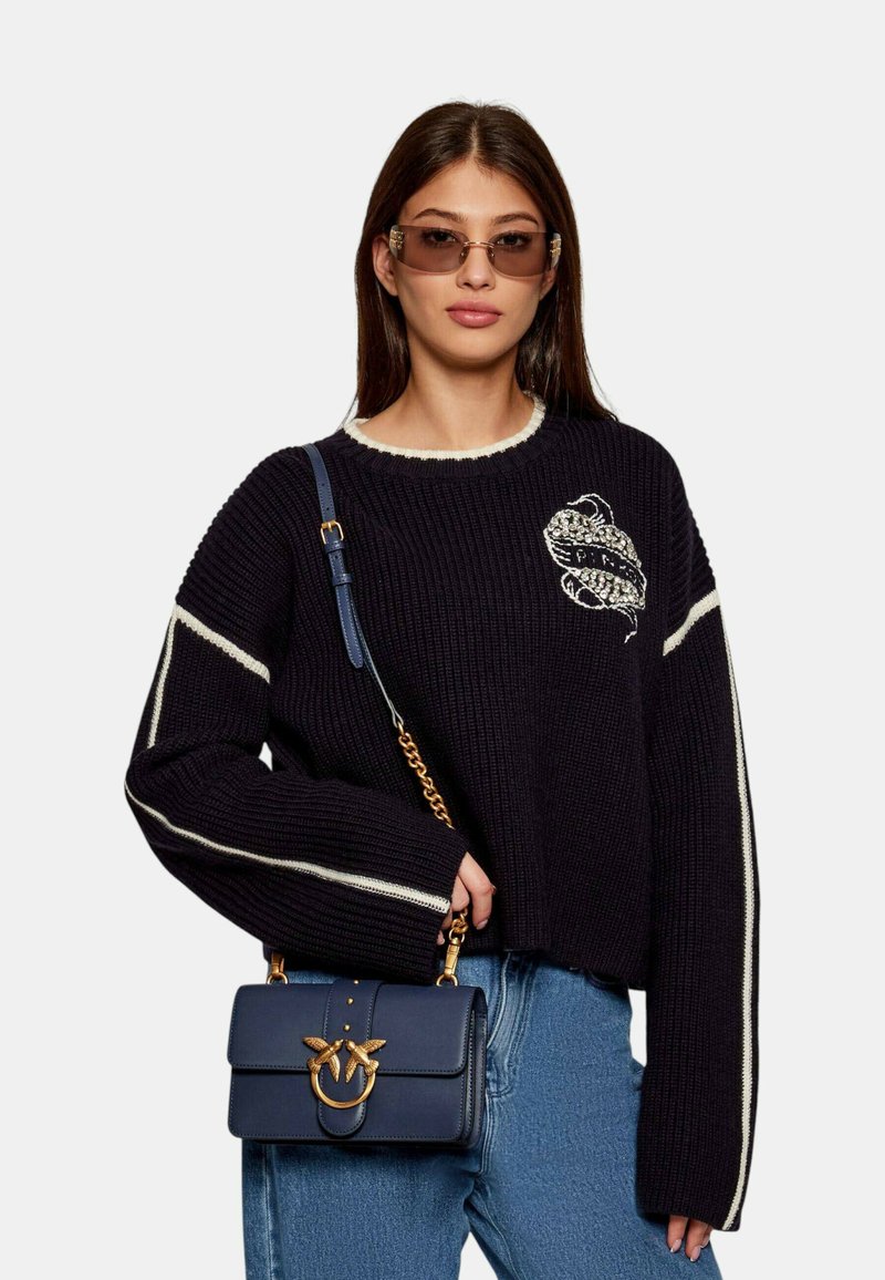 Maglione lavorato a maglia navy con strisce bianche e design ricamato, abbinato a una borsa strutturata navy con hardware dorato e tracolla a catena.