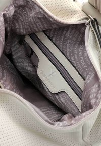 El interior del bolso de mano perforado en blanco presenta un forro gris suave con patrones de texto, un bolsillo con cremallera y una etiqueta de marca.
