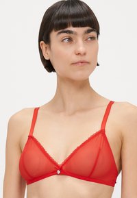 Rdeč prosojen nedrček v obliki trikotnika z čipkastim robom in osrednjim detajlom v obliki pentlje. Nastavljivi naramnice in gladka tekstura. Lahka tkanina z lesketajočim se videzom.