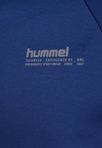 Blauwe stof met lichtgrijs "hummel" logo en tekst met de melding "Techwear - Ontworpen door HML, prestatiegerichte sportkleding sinds 1923."