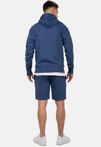 Blauwe katoenen hoodie met een kangoeroezak en ribgebreide boorden, gecombineerd met bijpassende shorts, tegen een neutrale achtergrond.