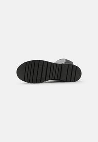 Suela de zapato de goma negra con un patrón texturizado, que presenta surcos y el logo grabado "TOMMY JEANS" cerca de la zona del talón.