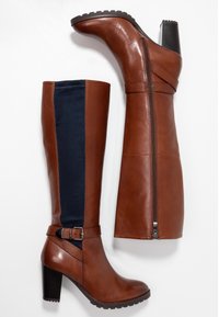 Botas de cuero marrón hasta la rodilla con un panel de tela azul marino, acento de hebilla y tacón negro texturizado. Cuenta con una cremallera lateral para un uso fácil.