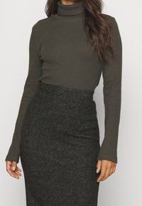 Haut en turtleneck côtelé vert foncé associé à une jupe crayon noire texturée, avec des manches longues et une silhouette ajustée.