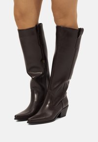 Braune kniehohe Lederstiefel mit spitzer Zehenpartie. Mit einem seitlichen Reißverschluss und dezentem dekorativem Nähen entlang des Schafts. Blockabsatz.